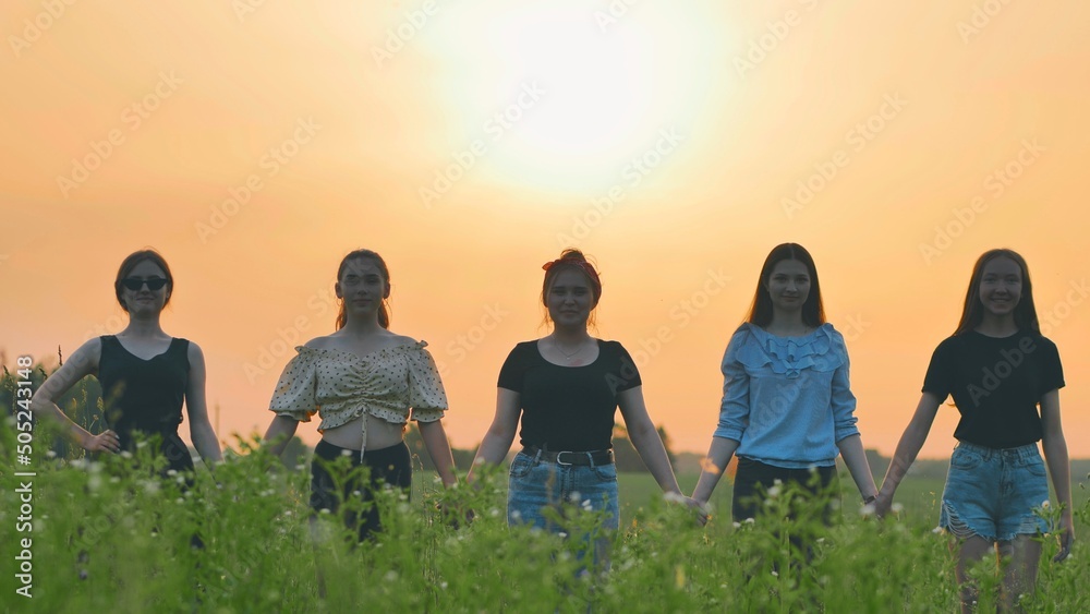 Fototapeta premium Girls stand holding hands at sunset on a summer evening.