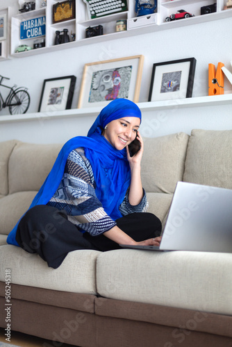 Smiling young Muslim woman using her laptop computer. Work from home, business, entrepreneurs.