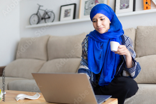 Young Muslim woman using her laptop. Working from home, studying online, browsing the Internet. Space for text.