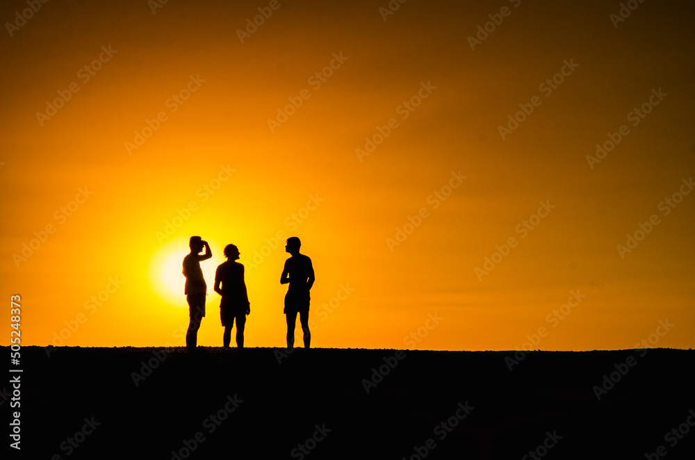 Silhouette of three persons with the sun falling in the background