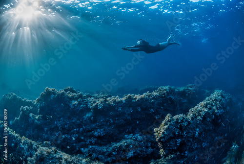 Girl swimming underwater in a rocky bottom with sunbeams coming from the left