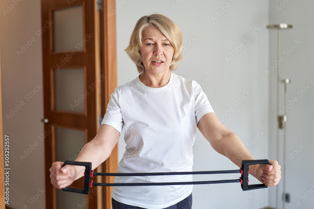 Obraz premium beautiful mature woman doing exercises for arm muscles using elastic band