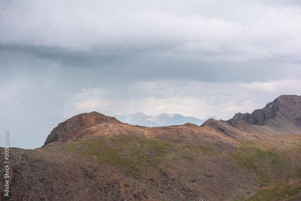 Dramatic aerial landscape with sunlit mountain top during rain at changeable weather. Atmospheric mountain scenery with sharp rocks in sunlight under lead gray cloudy sky. Rainy clouds in mountains.