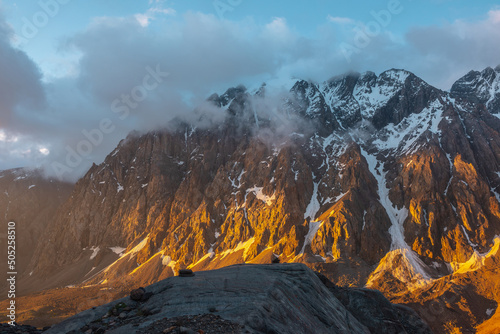 Scenic landscape with snowy mountain top in low clouds in golden sunrise colors. Colorful view to snow mountains and rocks in gold morning sunlight in low clouds. Awesome scenery with golden rocks. photo