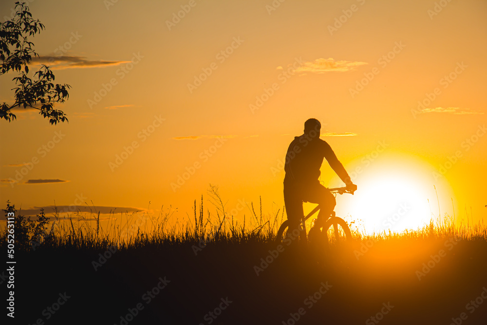 A cyclist rides through a field against the backdrop of a beautiful contour sunset light. Beautiful sunset. Photo of nature. Velotheme. A cyclist rides through a field against the backdrop of a beautiful contour sunset light. Beautiful sunset. Photo of nature. Velotheme.