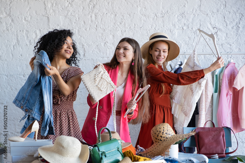 Obraz premium Happy women at swap party. Choose casual clothes, shoes, hats, bags, jewellery. Idea of exchange your old wardrobe for new. Eco friendly cloth concept. Zero waste shopping, reduce and reuse, donation