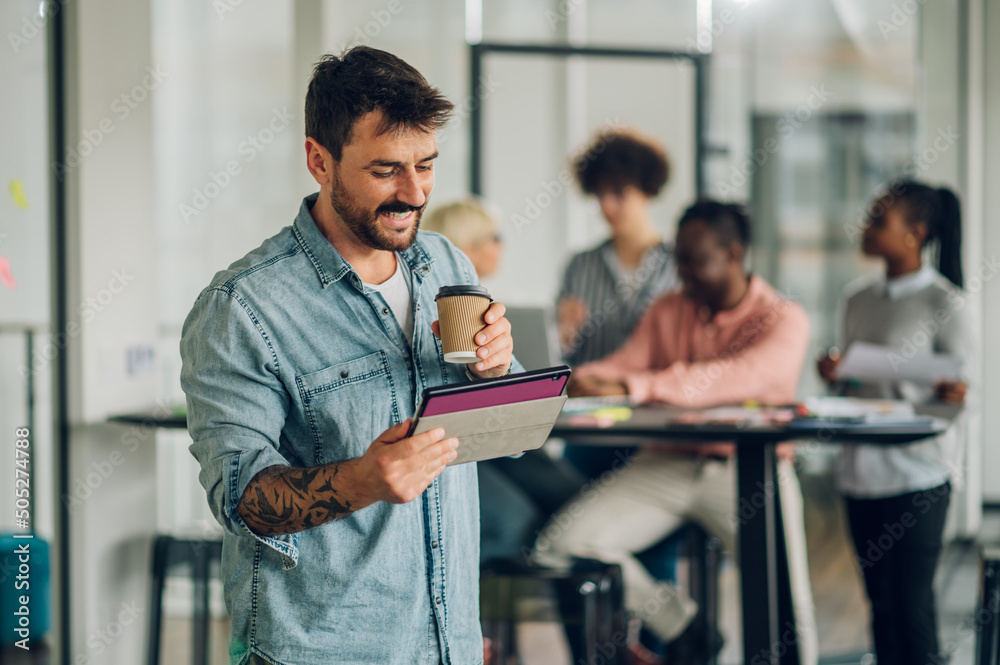 Business man using tablet in the office with his team working in the back Business man using tablet in the office with his team working in the back