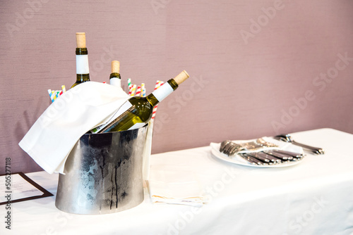 Tres botellas de vino blanco en un cubo con hielos para mantenerlas a una temperatura fría. Mesa con cubitera y cubiertos preparada para la recepción de una boda. photo