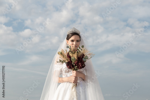 Uma jovem mulher usando um vestido de noiva com céu nublado ao fundo. photo
