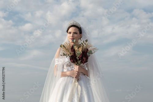 Uma jovem mulher usando um vestido de noiva com céu nublado ao fundo. photo