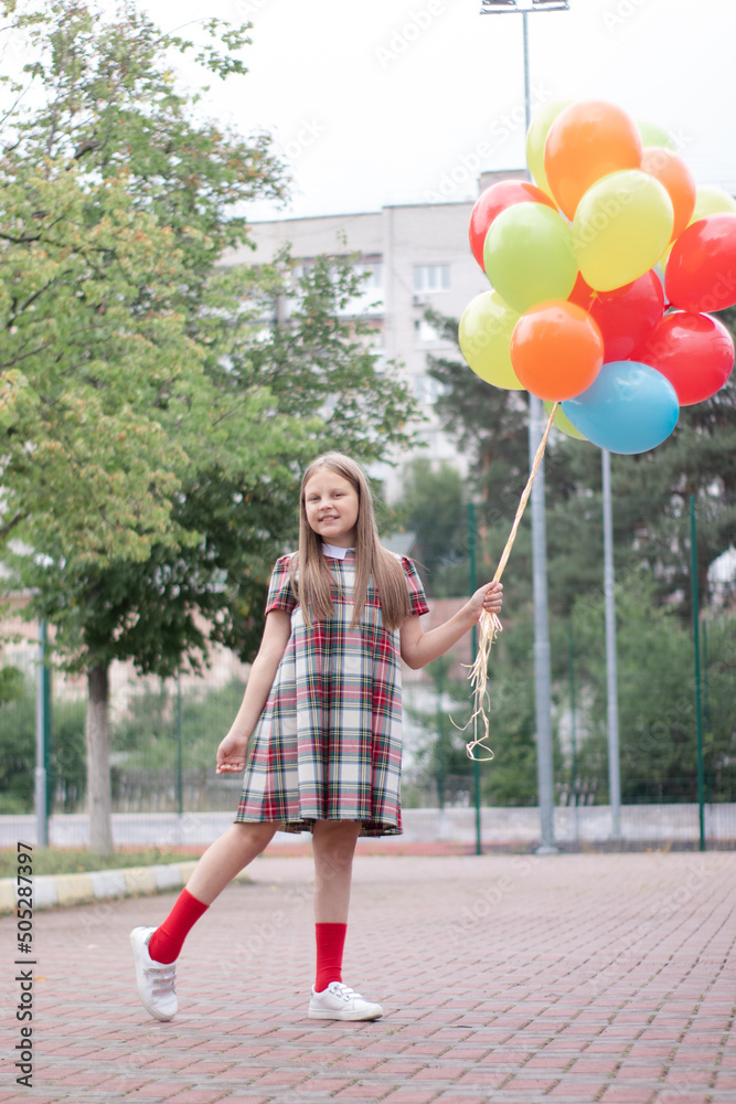 charming teenage girl in checkered brown dress with bunch of colorful balloons. school girl. pretty tween