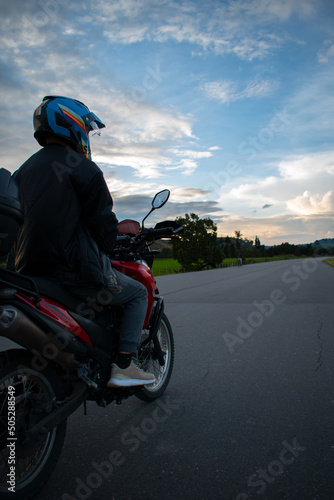 Fototapeta Naklejka Na Ścianę i Meble -  hombre conduciendo una moto roja y casco azul, con fondo de naturaleza