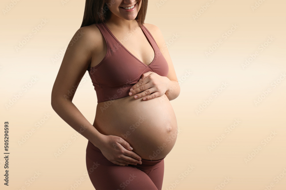 Young pregnant woman touching her belly on beige background, closeup Young pregnant woman touching her belly on beige background, closeup