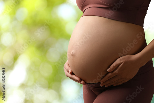 Young pregnant woman touching her belly outdoors, closeup. Space for text