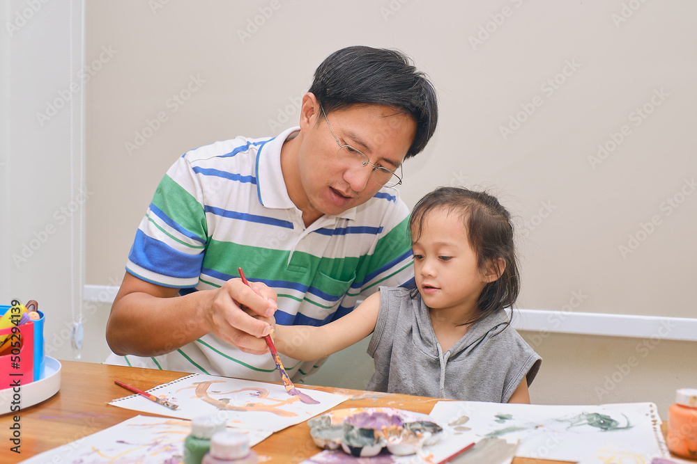 Asian father and child painting with paintbrush and watercolors at home, Dad and daughter spending quality time together, Learning at home, Homeschooling, Creative play for toddlers concept Asian father and child painting with paintbrush and watercolors at home, Dad and daughter spending quality time together, Learning at home, Homeschooling, Creative play for toddlers concept