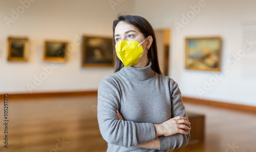 Interested woman tourist in protective mask admiring artworks at paintings exposition in art museum. Precautions in coronavirus pandemic photo