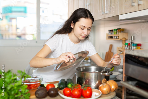 Portrait of young positive woman with saucepan of tasty hot soup in kitchen, cooking concept photo