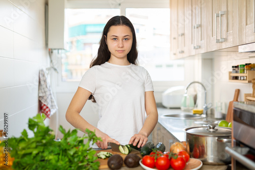 Young smiling woman chopping vegetables preparing healthy food at home kitchen photo