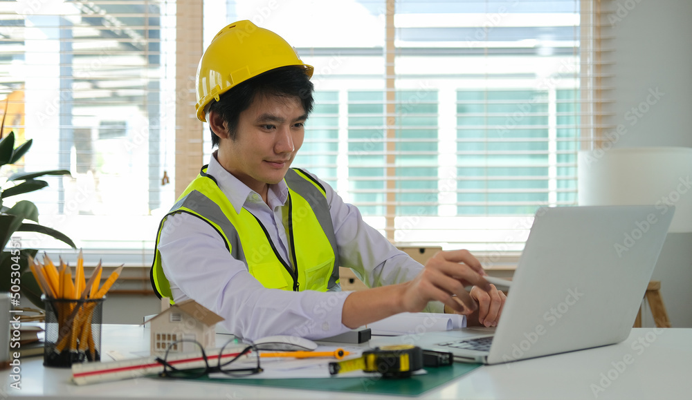 Professional Asian male architect using laptop computer, working on construction plan at his workplace. Professional Asian male architect using laptop computer, working on construction plan at his workplace.