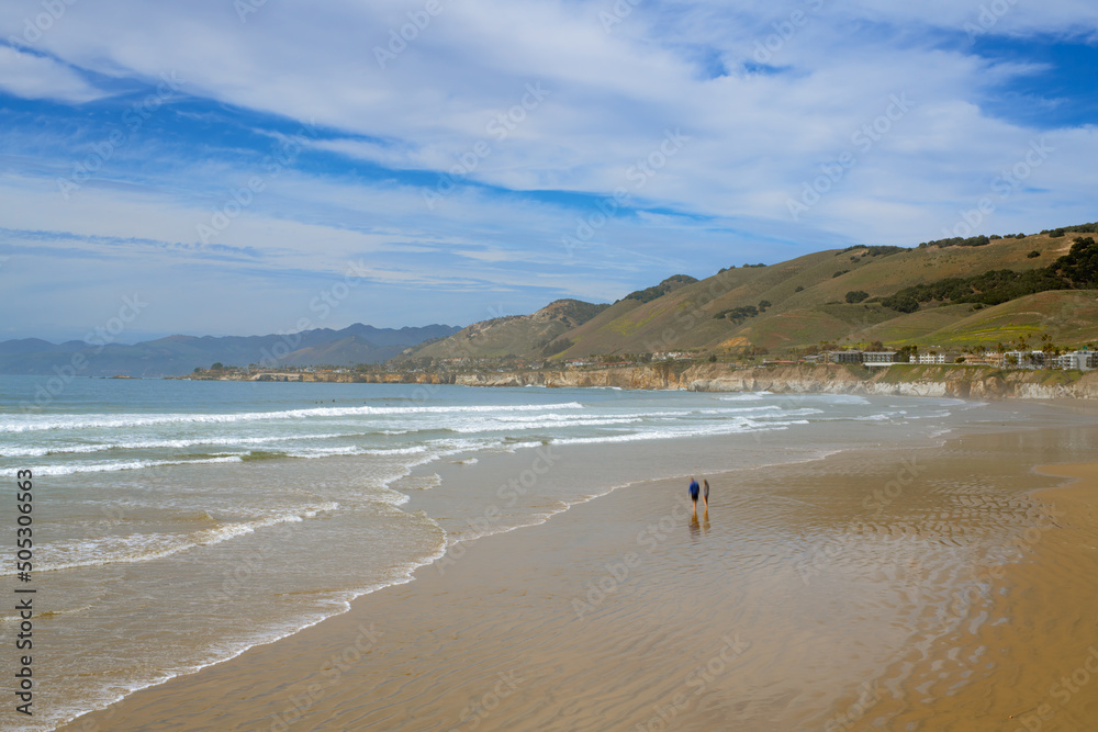 Wide sandy beach and oceanview, green hills and cloudy sky on background, California