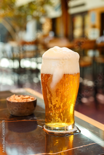 A tall transparent glass with fresh beer and nuts on a table in a street cafe