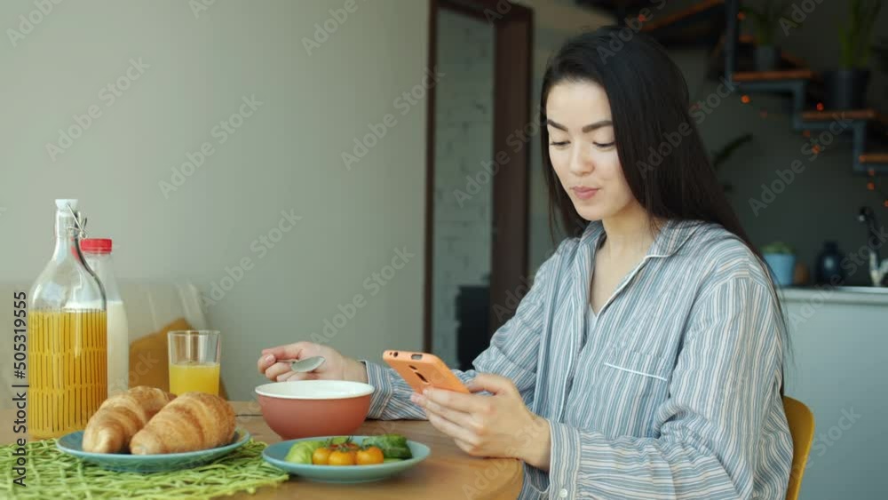 Portrait of young Asian woman having breakfast and using smartphone indoors in kitchen at home. Healthy food and joyful people concept. Portrait of young Asian woman having breakfast and using smartphone indoors in kitchen at home. Healthy food and joyful people concept.