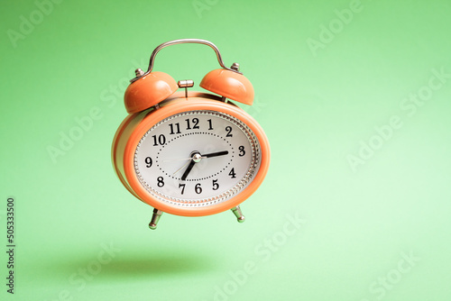 Orange vintage style flying alarm clock. Flying alarm clock on green background.