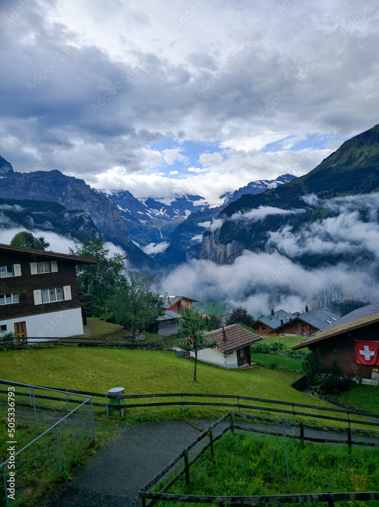 Fototapeta premium Lauterbrunnen, Switzerland - August 19, 2019: Beautiful view of the Alpine Lauterbrunnen valley with wooden chalets in the Jungfrau region. White clouds cover the mountains. Vertical