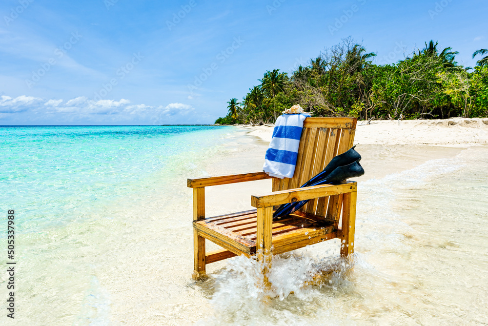 A wooden chair standing in the Indian Ocean with a towel, shell and flippers.