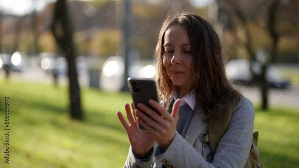 A middle-aged woman using a smartphone while walking down the street. Technologies, communications, business concept A middle-aged woman using a smartphone while walking down the street. Technologies, communications, business concept