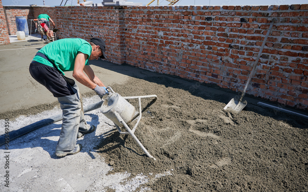 Male worker using concrete screed mixer machine while preparing sand-cement mix for floor screed. Man builder working with professional floor screed equipment at construction site. Male worker using concrete screed mixer machine while preparing sand-cement mix for floor screed. Man builder working with professional floor screed equipment at construction site.