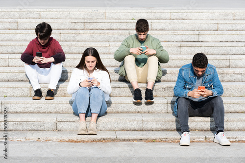 Teenager friends sitting on stairs and using their phones. Digital addiction and social distancing concept. photo