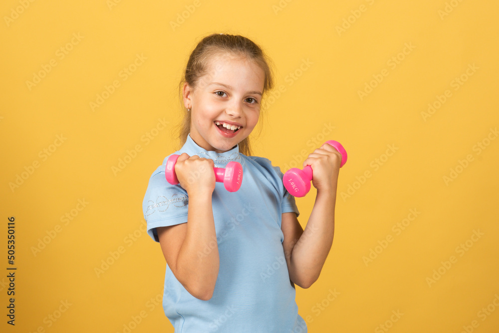 Cute little girl doing exercises with dumbbells in yellow background. Closeup portrait of sporty child with dumbbells. Happy child girl exercising. Cute little girl doing exercises with dumbbells in yellow background. Closeup portrait of sporty child with dumbbells. Happy child girl exercising.
