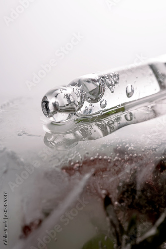 Pipette on a large piece of ice with frozen flowers.