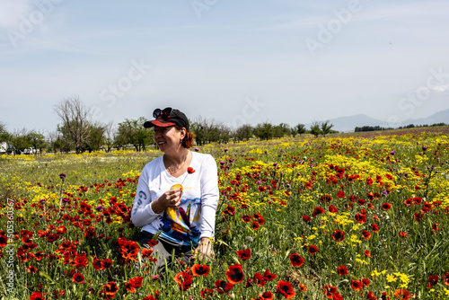 a woman in a cap and a white blouse sits on a poppy field among flowers on a sunny day