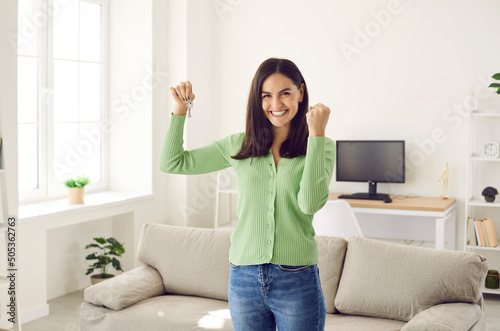 Portrait of satisfied lucky woman who is happy that she has finally become owner of her first new apartment. Woman with keys in hand looking at camera clenched fist and smiling broadly. photo