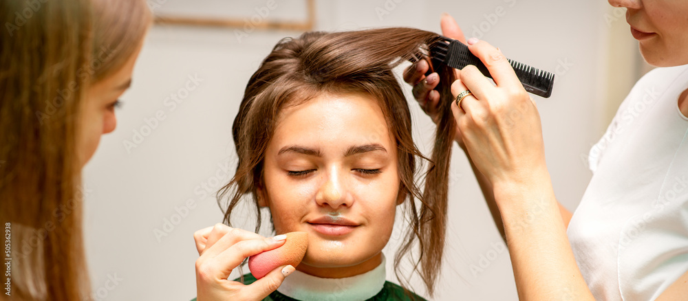 Fototapeta premium Makeup artist and hairdresser prepare the bride making hairstyle and makeup in a beauty salon