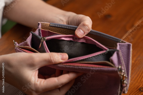 Woman opens empty wallet looking for money above table. Female hands hold violet purse on blurred background. Economical crisis concept closeup