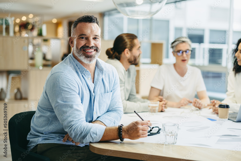Obraz premium Happy businessman sitting in a meeting with his colleagues