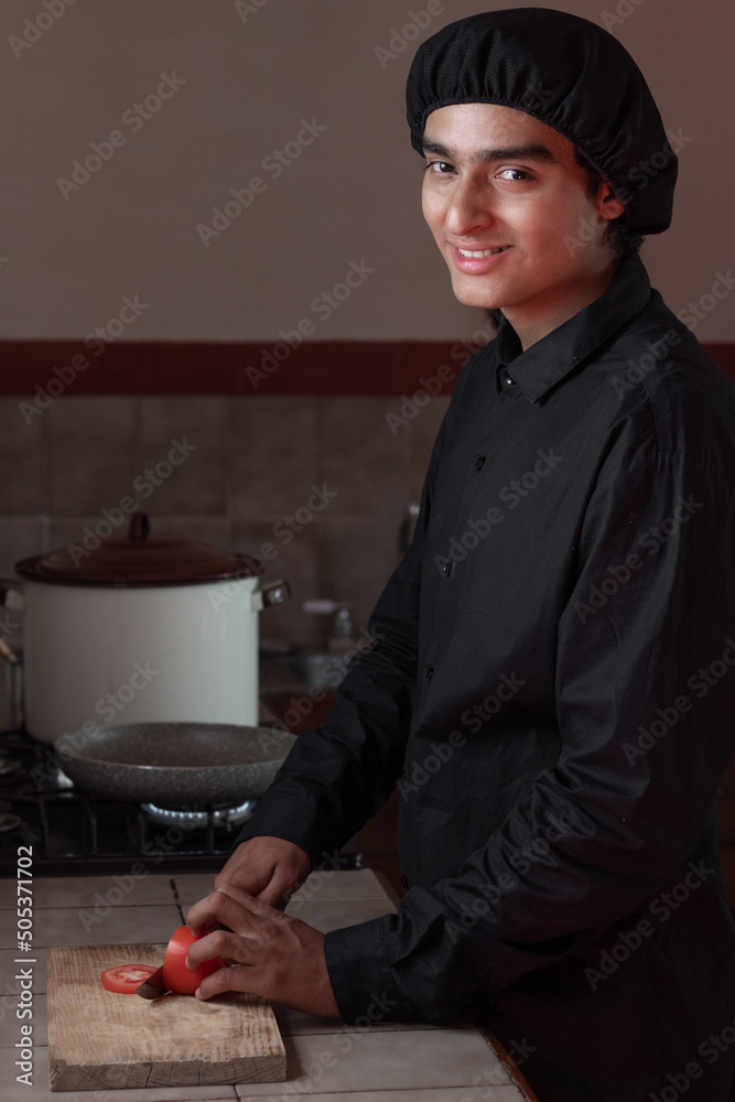 the young, smiling Arab chef has the pots on the stove while chopping fresh vegetables on the wooden board.