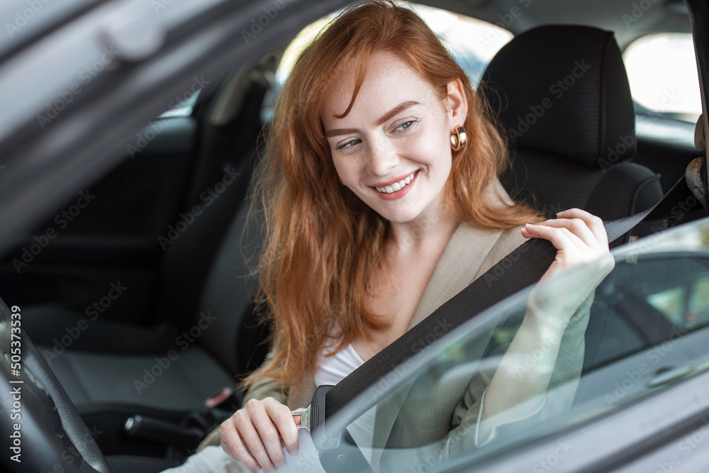 Young woman sitting on car seat and fastening seat belt, car safety concept. Woman fastens a seat belt in the car. Caucasian woman driver fastening car seat belt while sitting behind the wheel car.