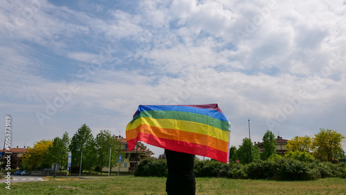 Bisexual, girl, lesbian, woman, transgender, homosexsual holding in hand a rainbow LGBT gender identity flag on sky background with clouds on a sunny day and celebrating a gay parade in pride month