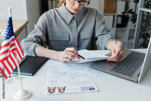 High angle shot of mature Caucasian woman wearing grau shirt sitting at desk in office working with visa application papers