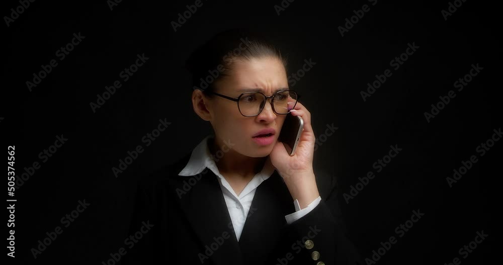 Business woman with glasses swears with a companion on a mobile phone, shouts into a smartphone. Facial expression with negative emotions. Isolated on a black background Business woman with glasses swears with a companion on a mobile phone, shouts into a smartphone. Facial expression with negative emotions. Isolated on a black background
