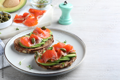 Delicious sandwiches with salmon, avocado and capers on white wooden table. Space for text