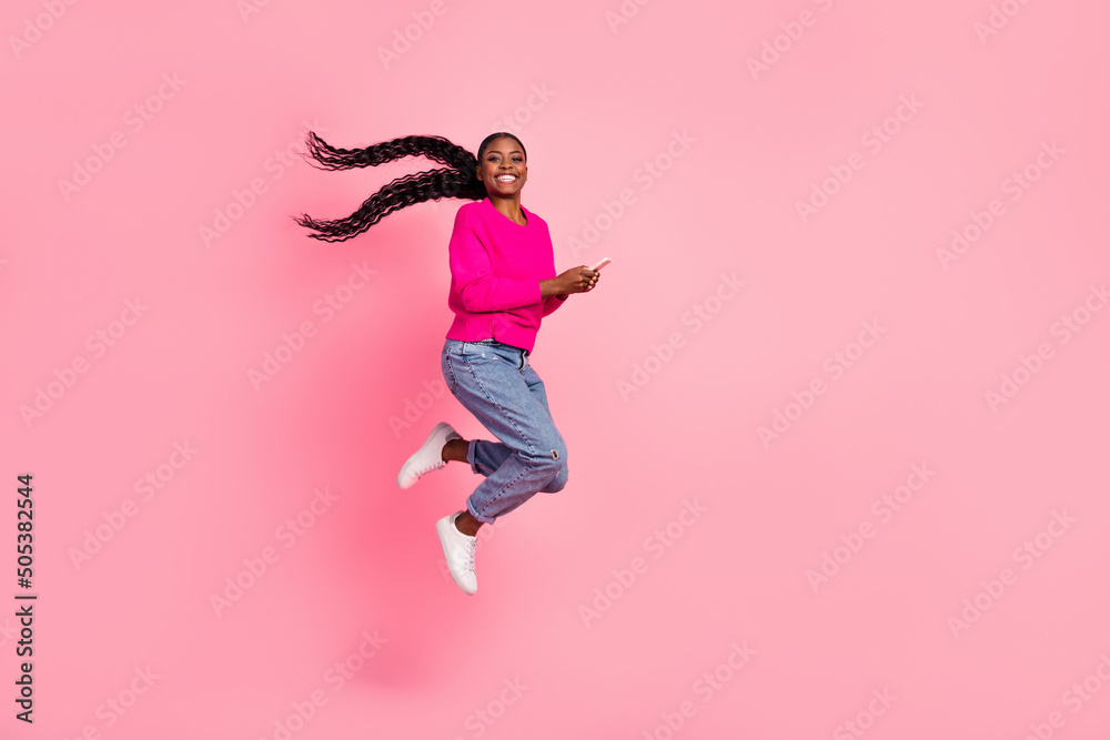 Full size photo of impressed millennial brunette lady hold telephone jump wear pullover jeans shoes isolated on pink background
