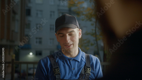 Young delivery man courier in blue cap into customer giving him a delivery slip to sign