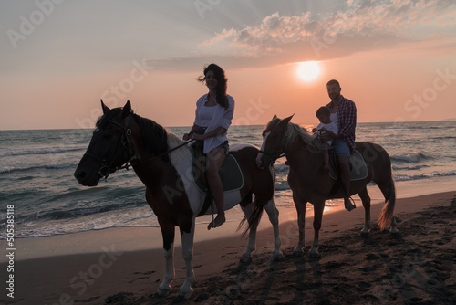 The family spends time with their children while riding horses together on a sandy beach. Selective focus 