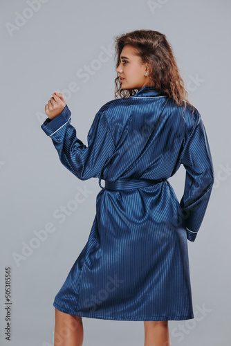 very sexy curly girl in a blue robe, night dress on a gray background. home clothes concept. catalog photo © Josep