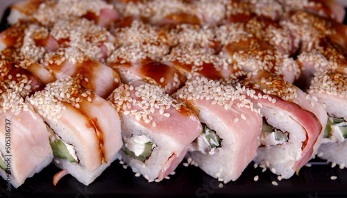 A portion of sushi with fish, rice and sesame seeds on a plastic backing.